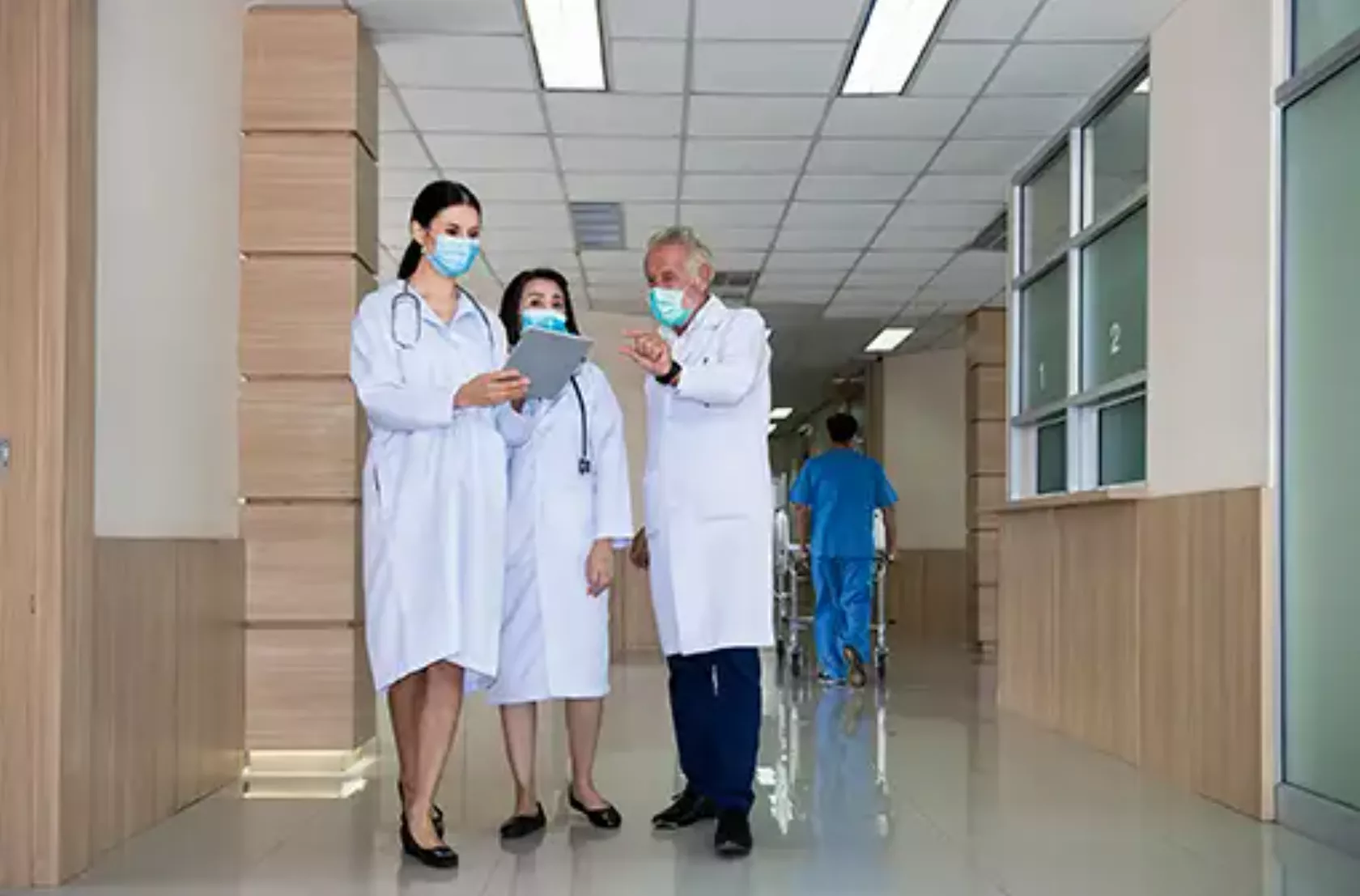 Eine Gruppe Ärztinnen und Ärzte mit OP-Masken diskutiert einen Fall auf dem Krankenhaus-Flur.
