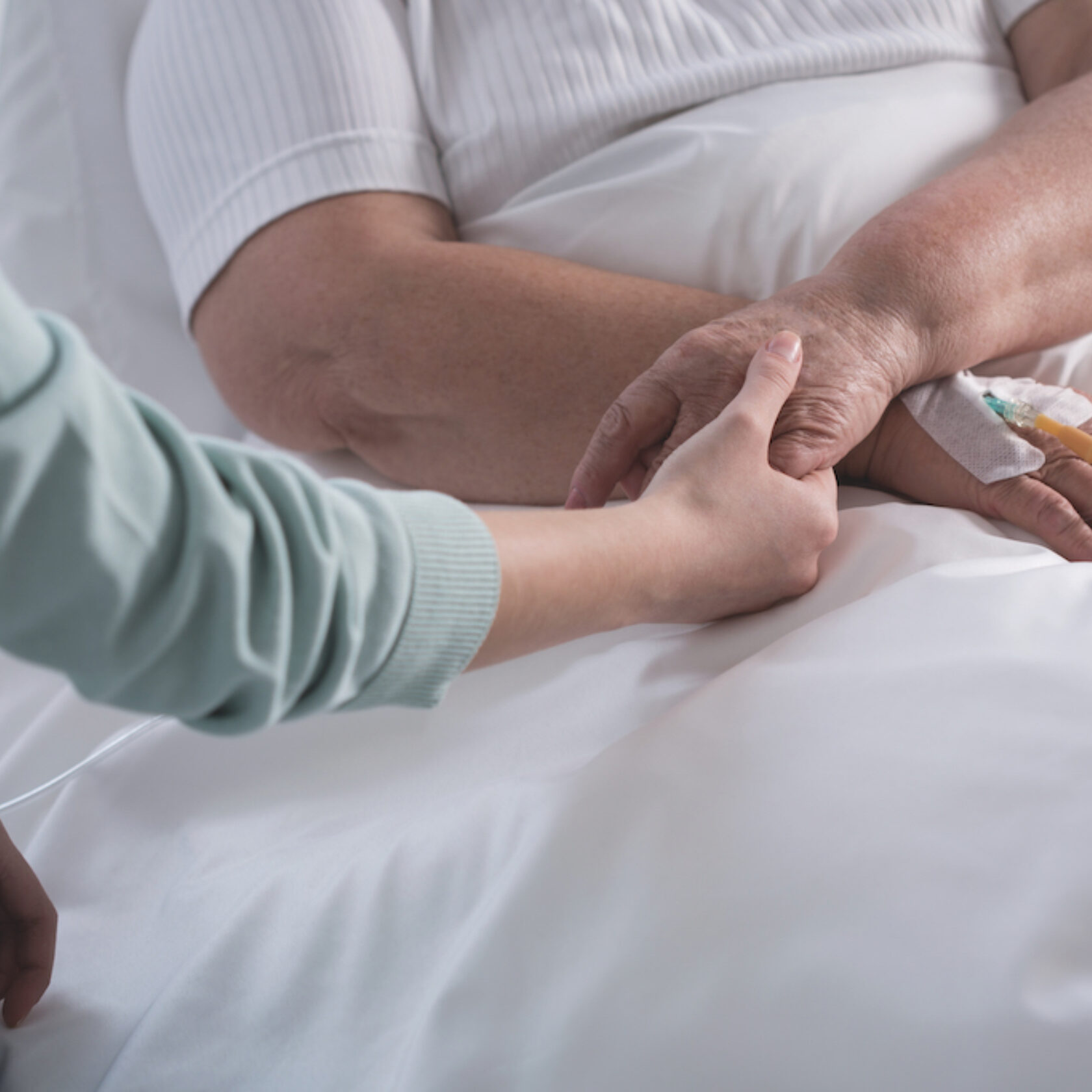 Palliativmedizinerin hält Patienten im Bett die Hand