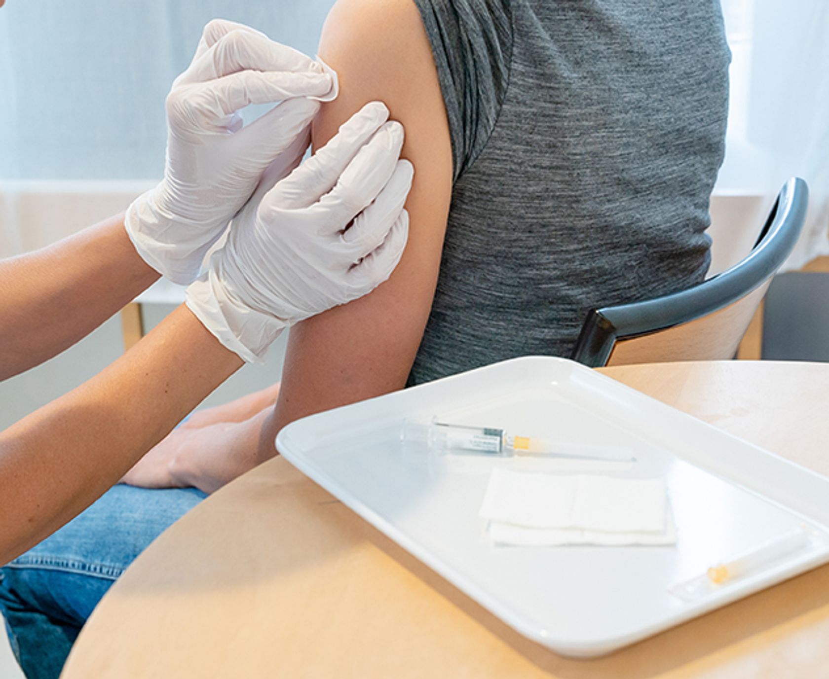 Hände einer Ärztin mit Handschuhen desinfizieren Oberarm einer Patientin nach einer Impfung.