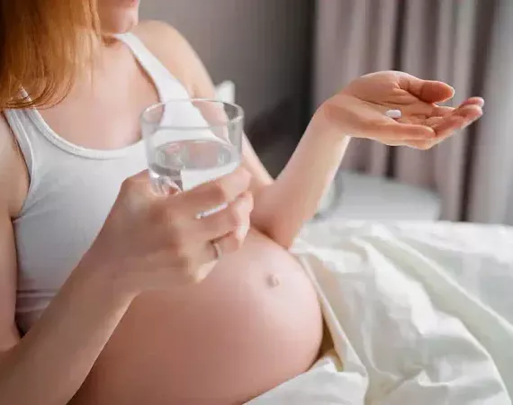 Schwangere hält eine Tablette und ein Glas Wasser.