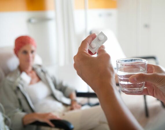 Frau bei der ambulanten Chemotherapie Hände mit Tabletten und Glas Wasser im Vordergrund