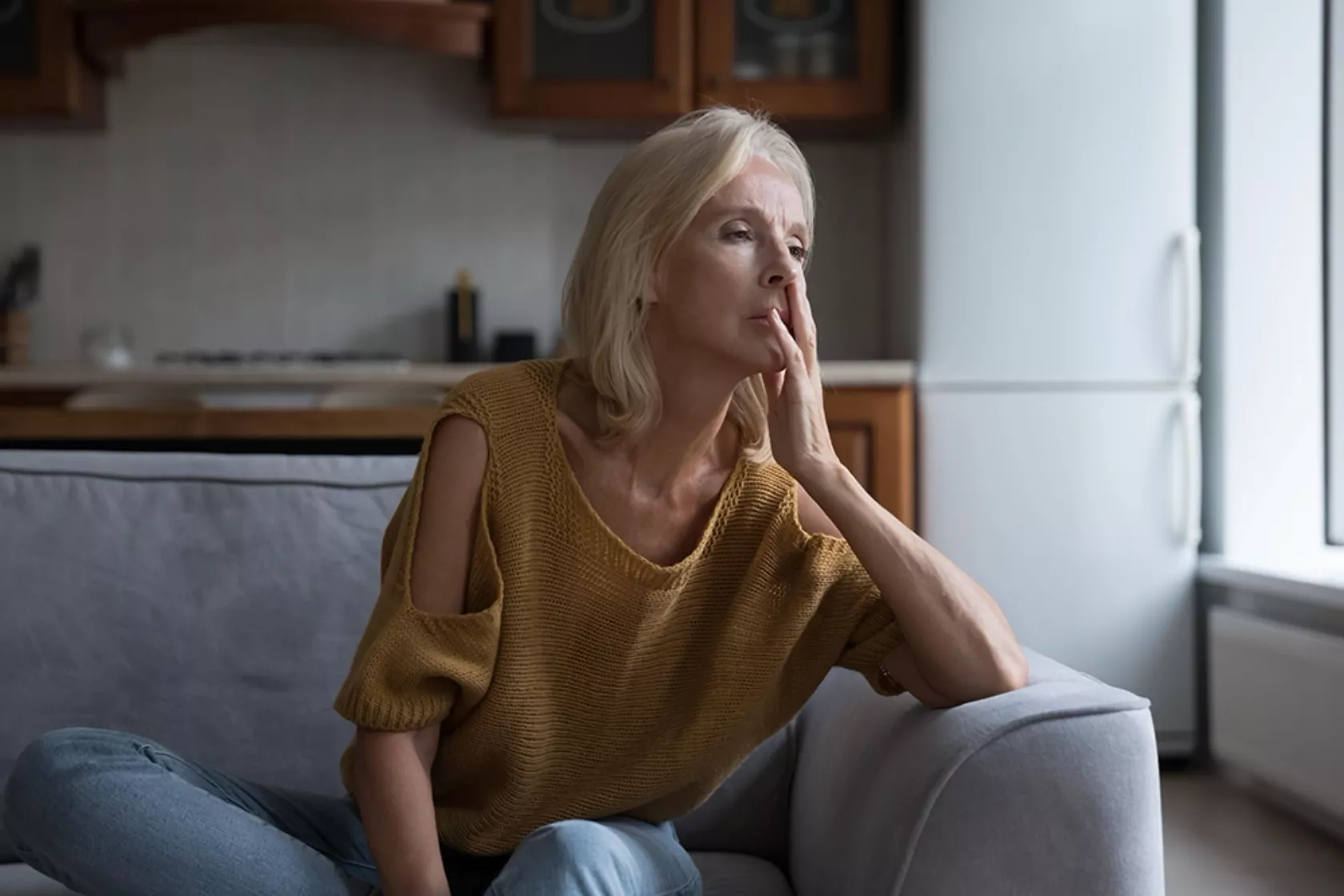 Frau in ihren 50ern sitzt frustriert blickend auf dem Sofa.